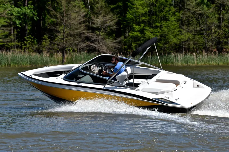 Slide: The Image of 2014 Regal 2100 boat cruising on a lake with lush green trees in the background. - 6