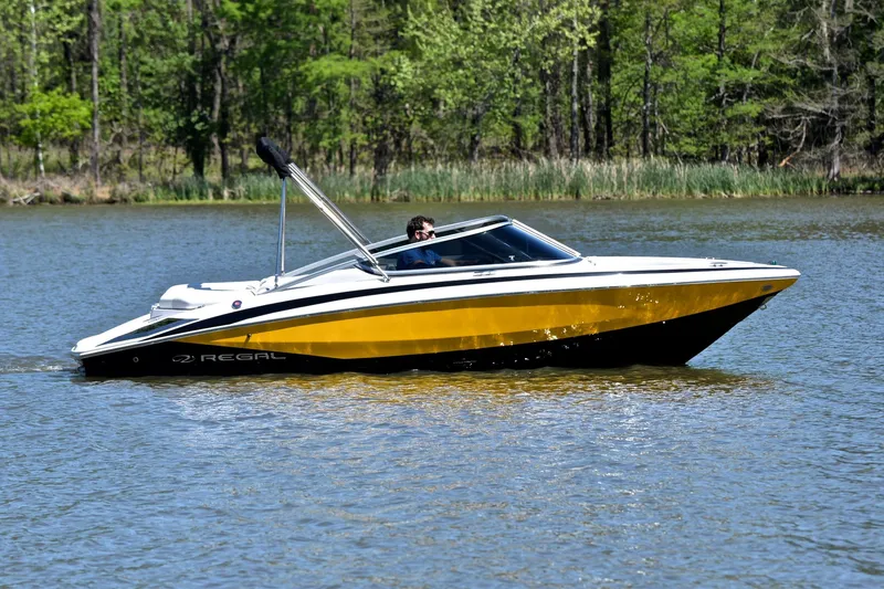 Slide: The Image of 2014 Regal 2100 boat cruising on a serene lake with lush green trees. - 7