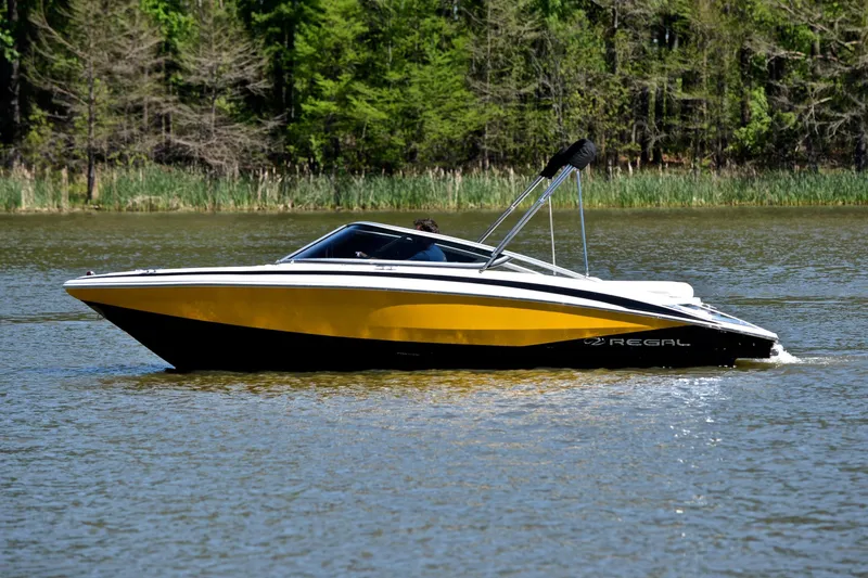 Slide: The Image of 2014 Regal 2100 boat cruising on a calm lake with lush green trees in the background. - 9