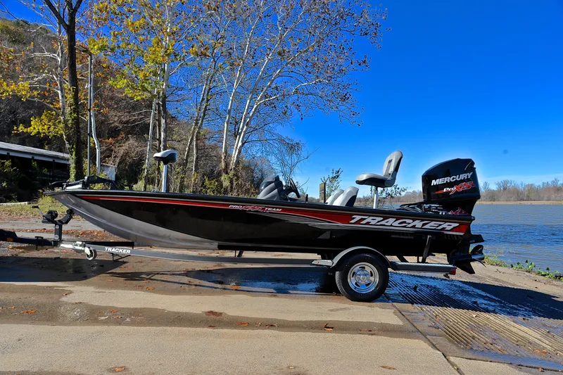 Slide: The Image of 2018 Bass Tracker Pro 19 boat on trailer by a lake, surrounded by trees. - 11