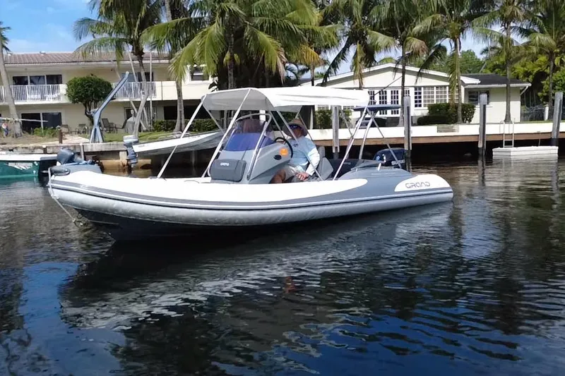 The Image of 2020 Grand Inflatables G580 boat cruising on calm water near a residential dock. - 1