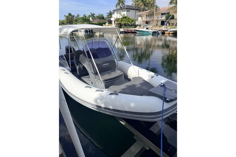 Slide: The Image of 2020 Grand Inflatables G580 boat docked by waterfront homes, featuring sleek design and canopy. - 11