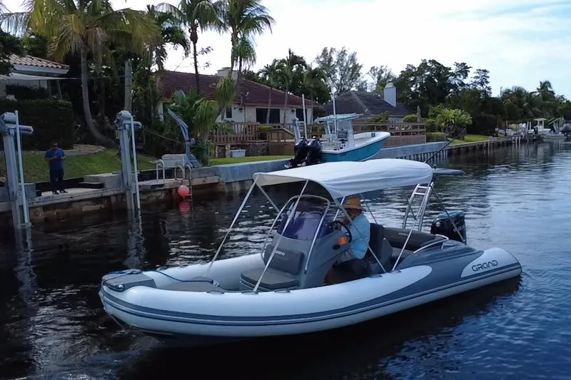 Slide: The Image of 2020 Grand Inflatables G580 boat cruising on a calm canal near waterfront homes. - 13