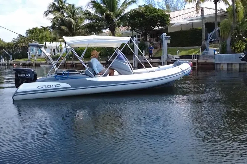 Slide: The Image of 2020 Grand Inflatables G580 boat on water, featuring Suzuki outboard motor, near dock. - 6