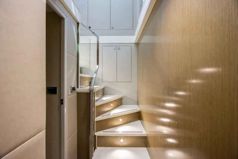 Slide: The Image of Staircase in 2017 Hatteras M75 Panacera yacht with modern wood paneling and ambient lighting. - 56