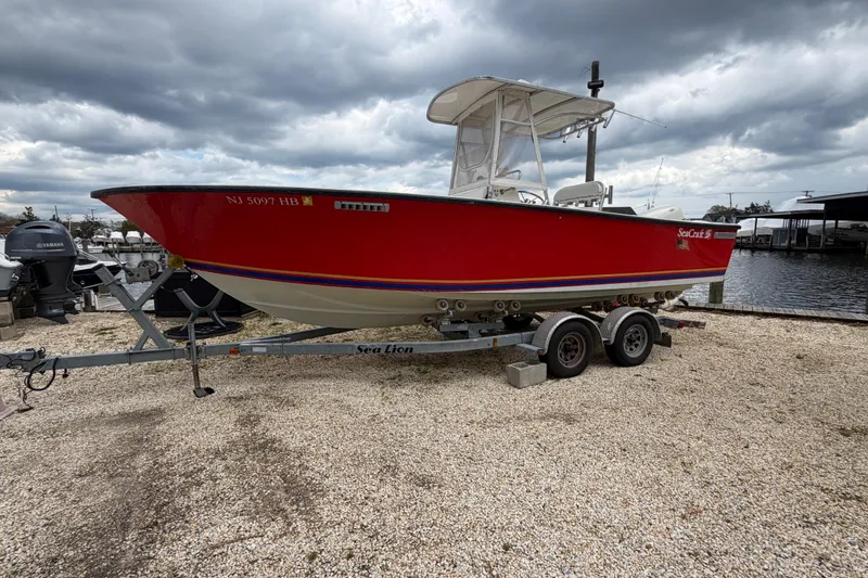 The Image of 1985 SeaCraft SC 23 Classic boat on trailer, red hull, parked near waterfront. - 0