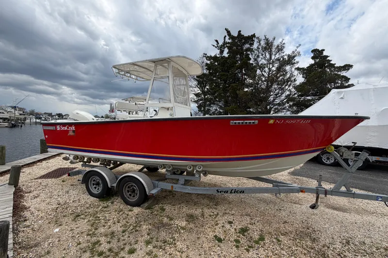 Slide: The Image of Red 1985 SeaCraft SC 23 Classic boat on trailer, parked near marina under cloudy sky. - 3