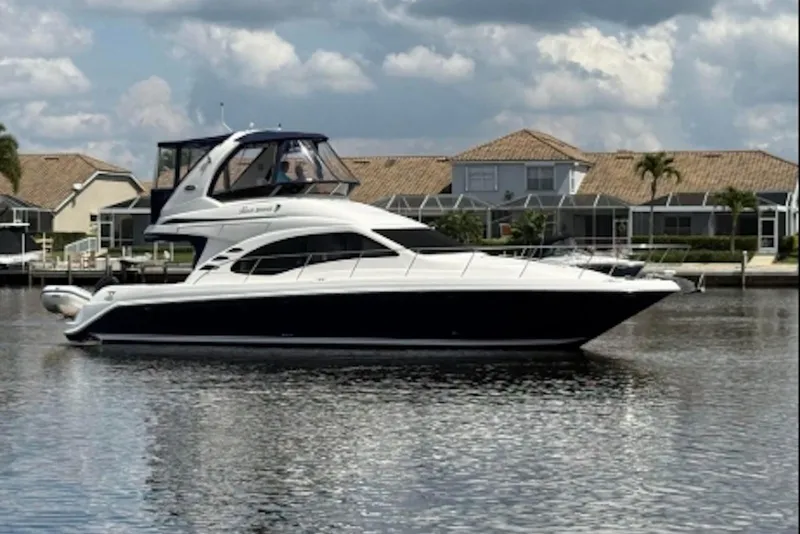 The Image of 2006 Sea Ray 44 Sedan Bridge yacht on calm water, with houses in the background. - 0