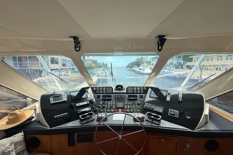 Slide: The Image of Cockpit view of 1990 Hatteras 58 Convertible yacht, showcasing navigation controls and waterfront scenery. - 10