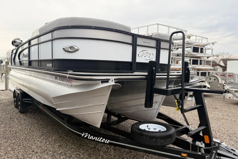 Slide: The Image of 2022 Manitou 230 Encore SL SHP pontoon boat on trailer, parked on gravel. - 2