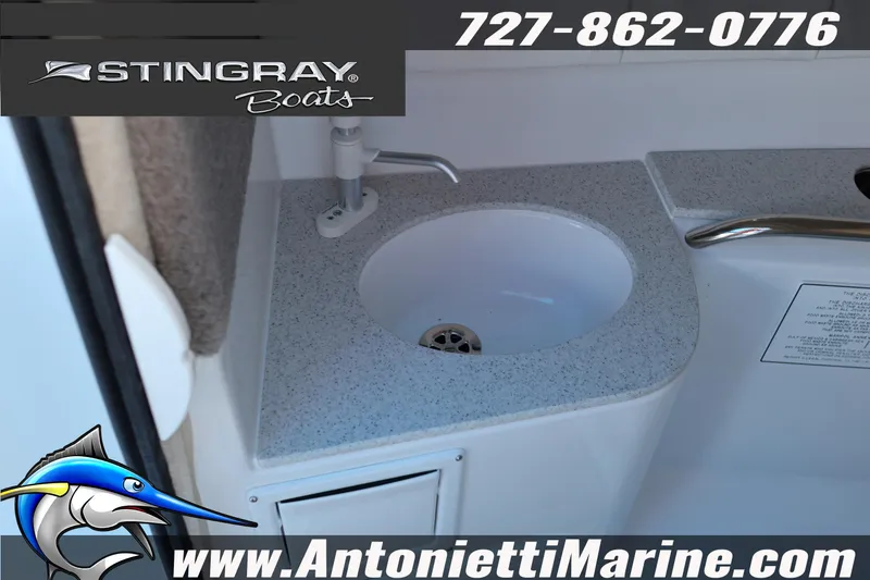 Slide: The Image of 2026 Stingray 211 DC boat interior sink with countertop, featuring marine branding and contact details. - 17