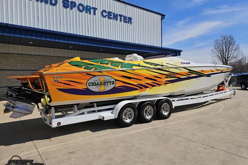 Slide: The Image of 2001 Cigarette 42' Tiger speedboat with vibrant graphics on a trailer outside a sport center. - 11