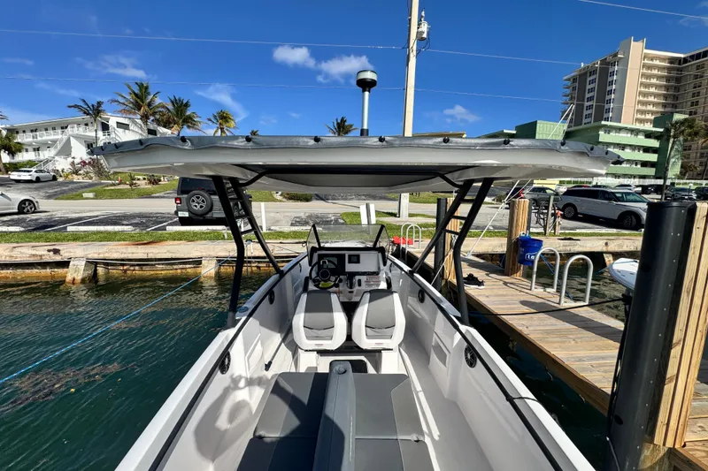 Slide: The Image of 2022 Axopar 22 T-Top boat docked, showcasing helm and seating area under sunny skies. - 2