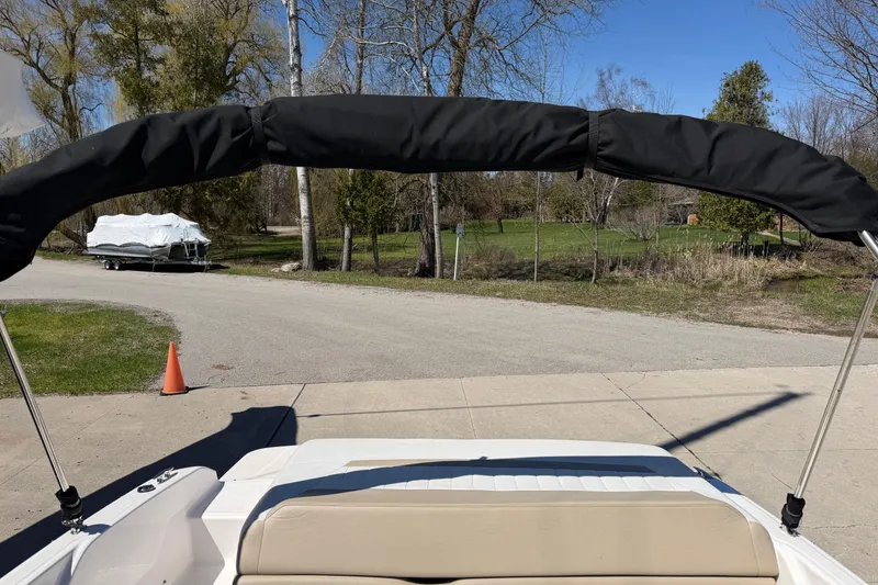 Slide: The Image of 2013 Regal 1900 Bowrider boat with bimini top, parked near trees and road. - 21