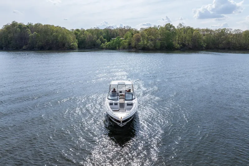 Slide: The Image of 2014 Chaparral 327 SSX boat cruising on a serene lake with lush green shoreline. - 3