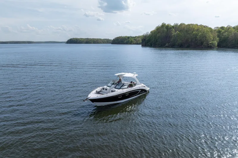 Slide: The Image of 2014 Chaparral 327 SSX boat cruising on a serene lake with lush green shoreline. - 4