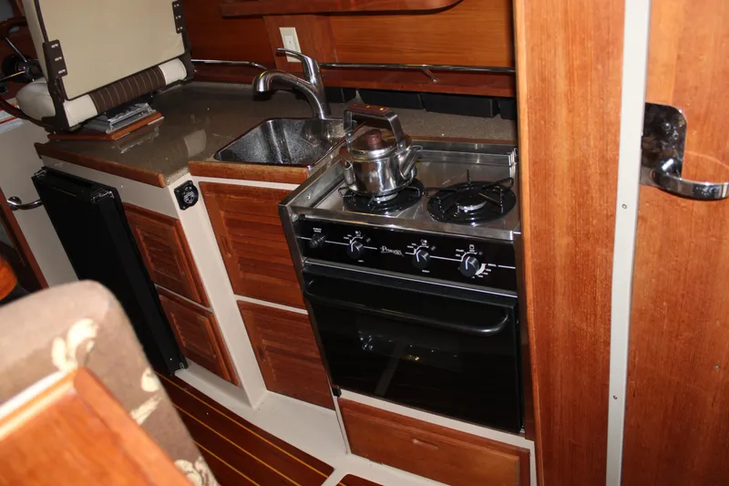 Slide: The Image of Compact kitchen in 2011 Ranger Tugs R-27 boat with stove, sink, and wooden cabinetry. - 26