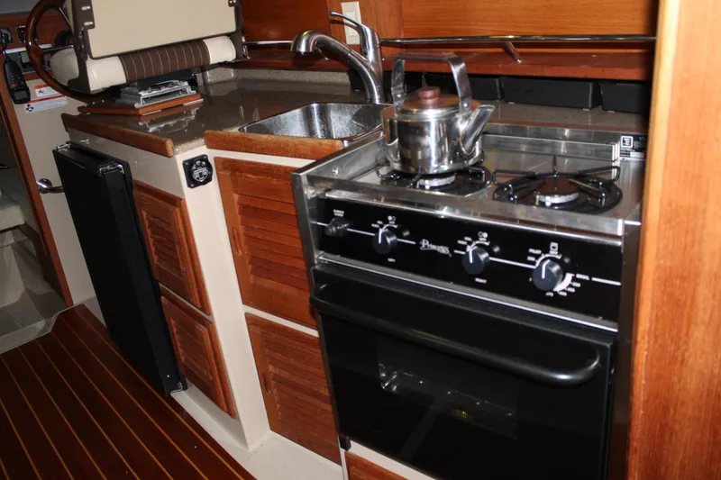 Slide: The Image of 2011 Ranger Tugs R-27 boat kitchen with stove, sink, and wooden cabinetry. - 32