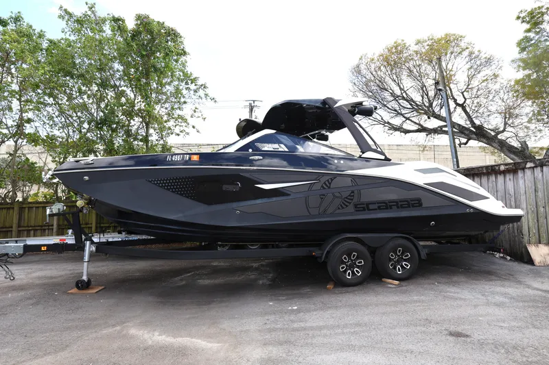 The Image of 2024 Scarab 285 ID boat on trailer, sleek black design, parked outdoors. - 0