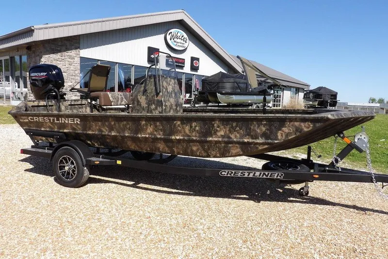 The Image of 2026 Crestliner 1860 Retriever CC Tunnel boat on trailer, camo design, parked outside dealership. - 1
