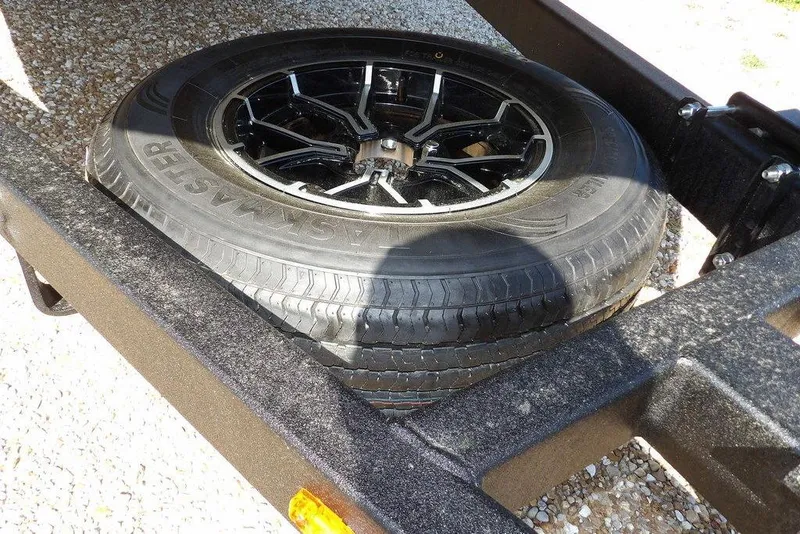 Slide: The Image of Spare tire on Crestliner 1860 Retriever CC Tunnel trailer, 2026 model, resting on gravel. - 25