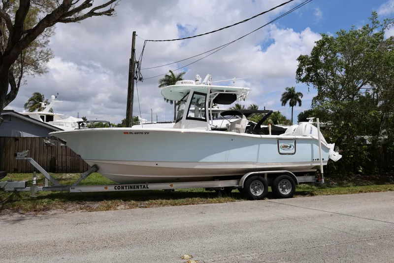 Slide: The Image of 2024 Sea Hunt Gamefish 25 boat on trailer, parked roadside under cloudy sky. - 6