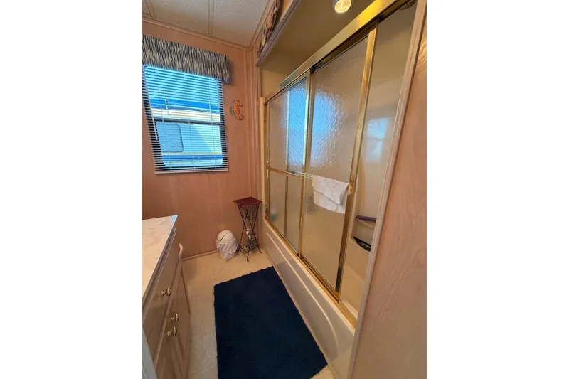 Slide: The Image of Bathroom with glass shower doors, blue rug, and window in a 2000 Sunstar 16x65 model. - 30