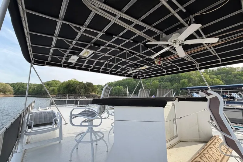 Slide: The Image of Upper deck of 2000 Sunstar 16x65 houseboat with seating and ceiling fan, docked by a lake. - 43