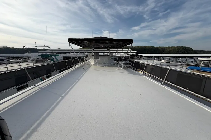 Slide: The Image of Sunstar 16x65 houseboat deck, 2000 model, with chairs under a canopy, docked by the lake. - 51