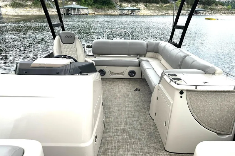 Slide: The Image of 2018 Harris Grand Mariner 250 pontoon boat interior with plush seating and helm, docked on a lake. - 4