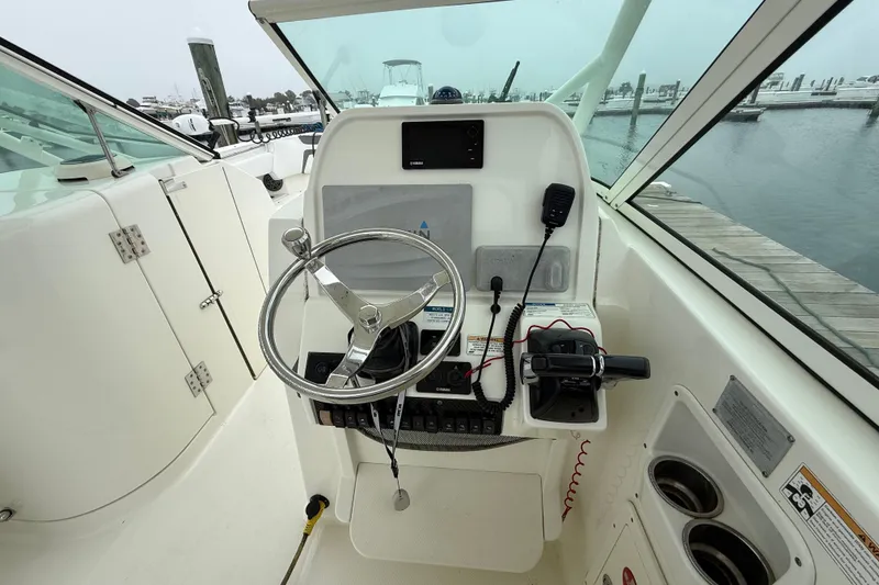 Slide: The Image of 2018 World Cat 295 DC boat helm with steering wheel, controls, and dockside view. - 7