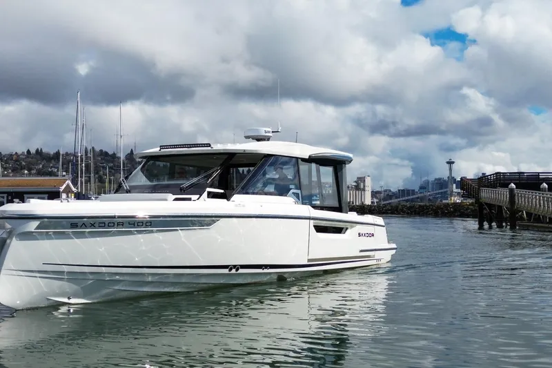 Slide: The Image of 2026 Saxdor 400 GTC boat cruising near a city skyline under cloudy skies. - 1