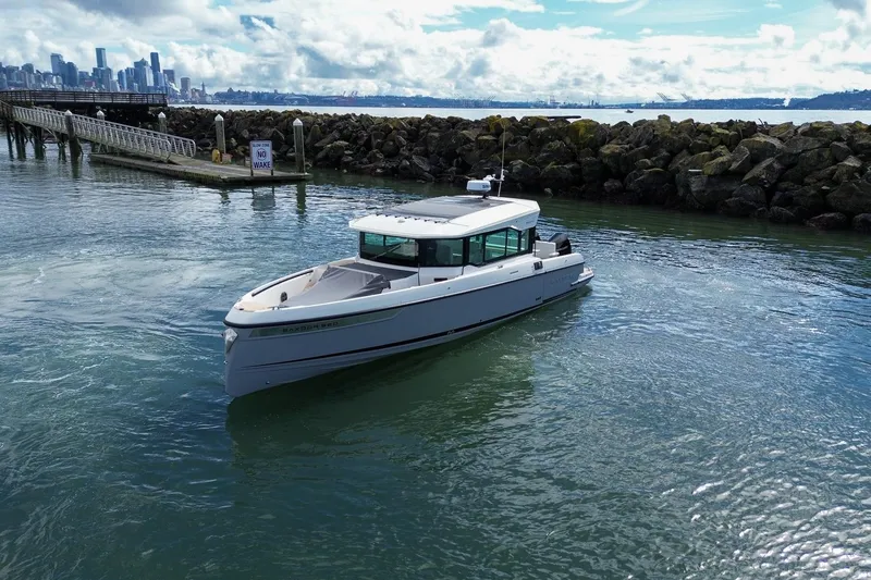 Slide: The Image of 2026 Saxdor 320 GTC boat cruising near rocky shoreline with city skyline in background. - 33