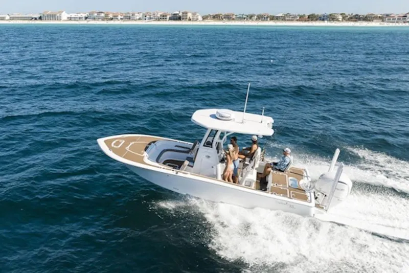 The Image of 2026 Tidewater 2500 Carolina Bay boat cruising on open water near a coastal town. - 1