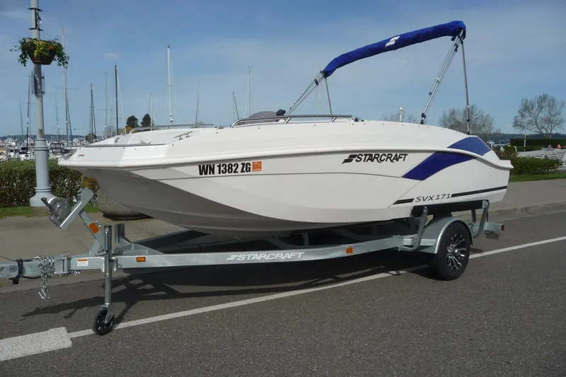 Slide: The Image of 2022 Starcraft SVX 171 OB boat on trailer, parked near marina with clear sky. - 10