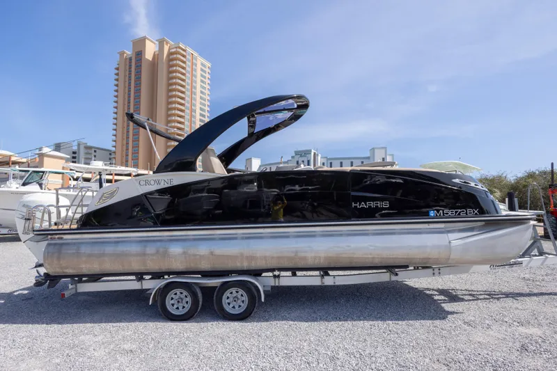 Slide: The Image of 2016 Harris Crowne 250 pontoon boat on trailer, urban backdrop, clear sky. - 4
