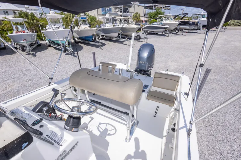 Slide: The Image of 2017 NauticStar 2400 Sport boat interior with steering wheel and seating, parked among other boats. - 23