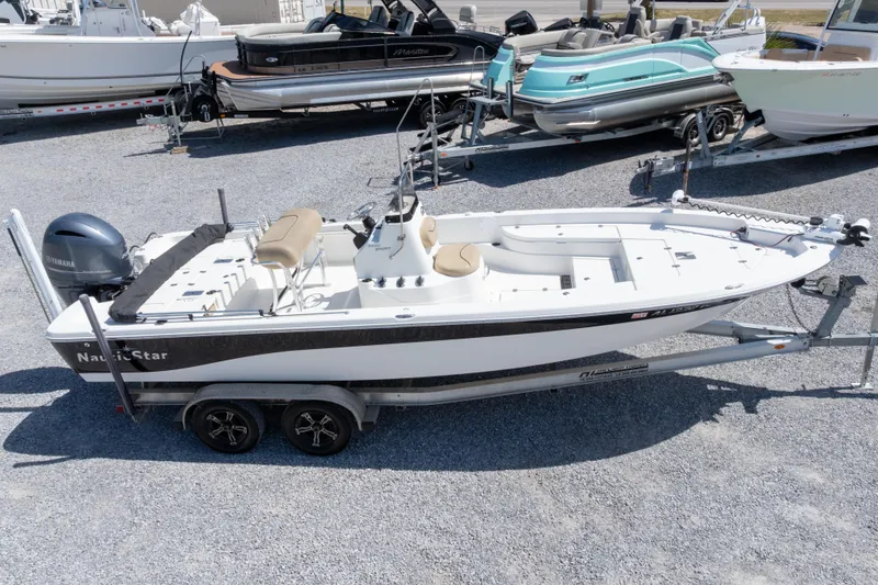 Slide: The Image of 2017 NauticStar 2400 Sport boat on trailer, parked among other boats. - 34