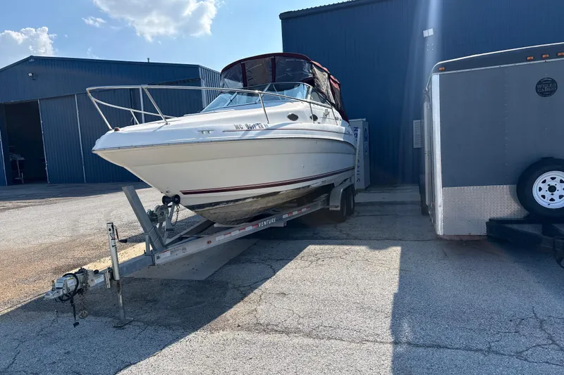 Slide: The Image of 1996 Sea Ray 240 Sundancer boat on trailer, parked near industrial buildings under a clear sky. - 7