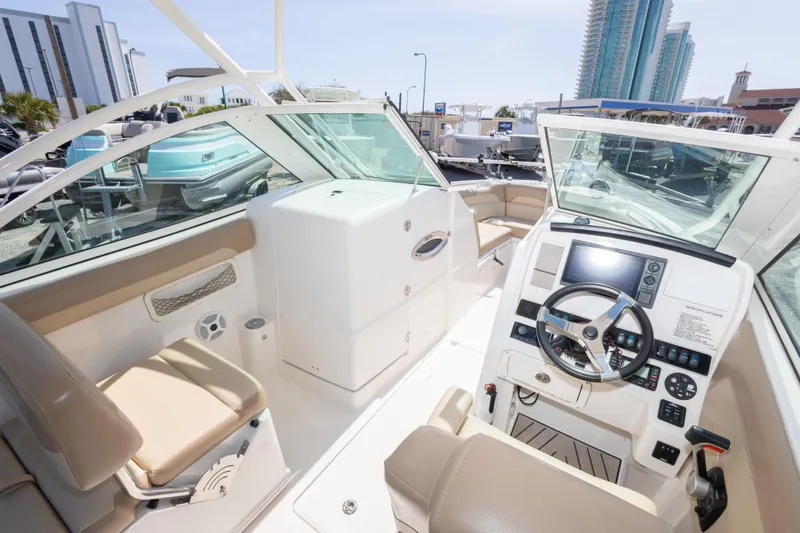 Slide: The Image of 2018 Sailfish 245 DC boat interior with modern dashboard and seating, docked near high-rise buildings. - 22