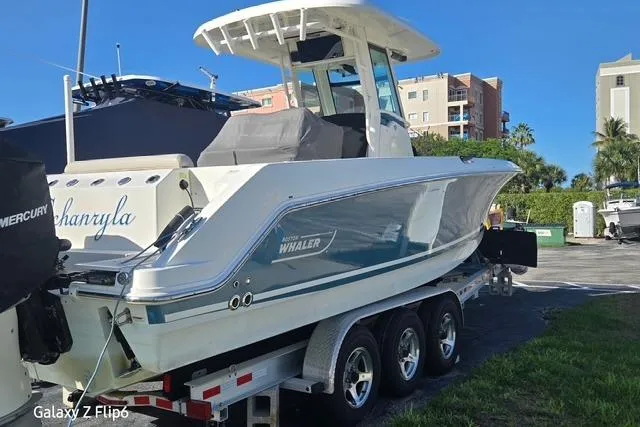 Slide: The Image of 2018 Boston Whaler 280 Outrage boat on trailer, parked outdoors under clear blue sky. - 2