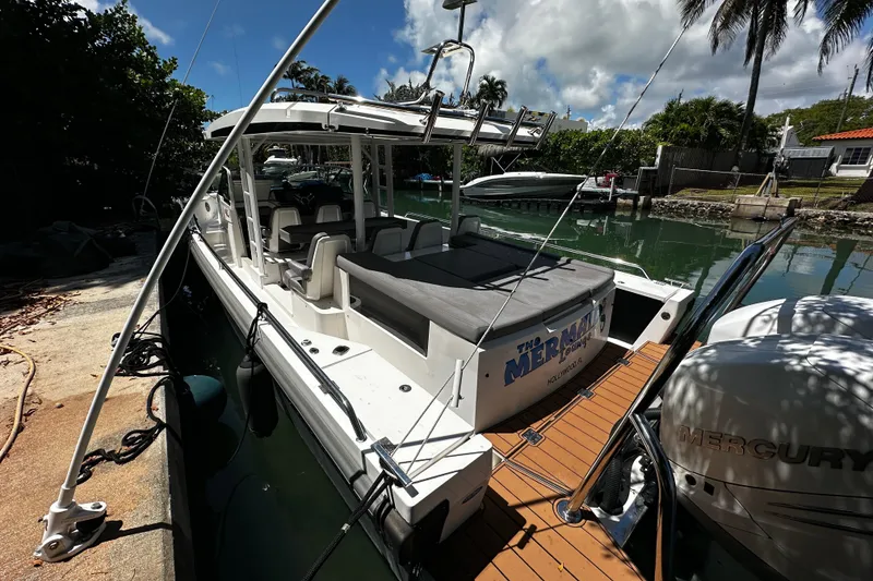 Slide: The Image of 2018 Axopar 37 Sun-Top boat docked by a canal, featuring a spacious deck and twin Mercury engines. - 20