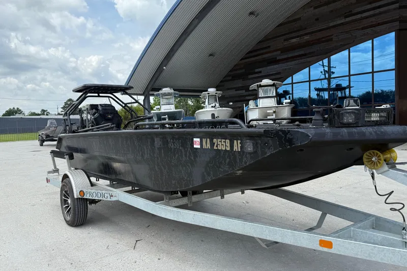 Slide: The Image of 2024 Prodigy 17 boat on trailer, parked outside modern building under cloudy sky. - 2