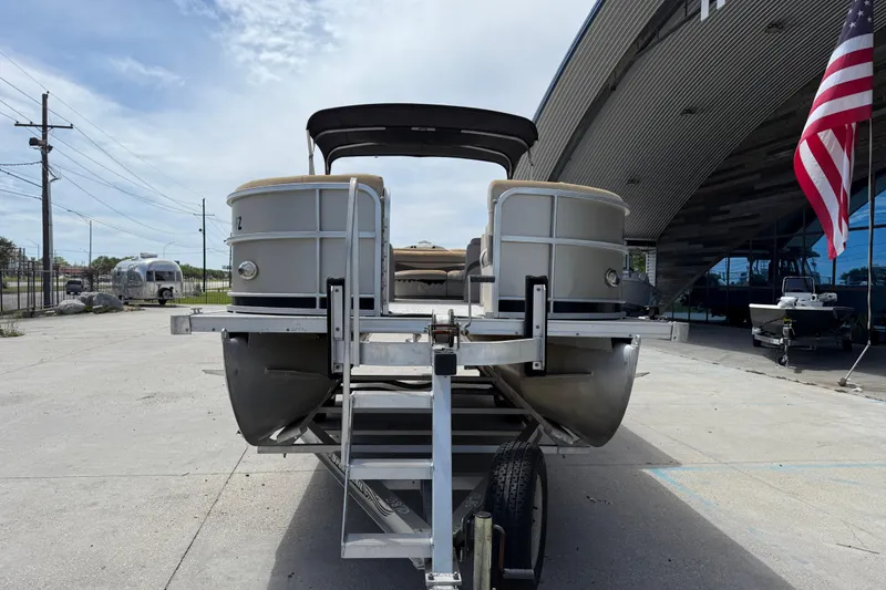 Slide: The Image of 2012 South Bay 522 CR pontoon boat on trailer, parked near modern building and American flag. - 8