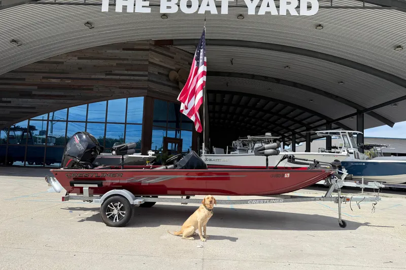 Slide: The Image of 2023 Crestliner 1850 SC boat on trailer with dog, American flag, and "The Boat Yard" sign. - 2