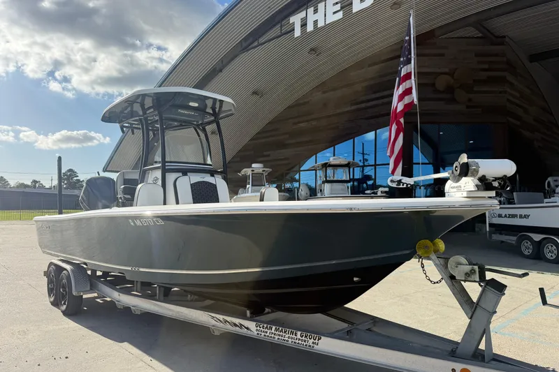 Slide: The Image of 2021 Tidewater 2500 Carolina Bay boat on trailer, parked outside a building with an American flag. - 6