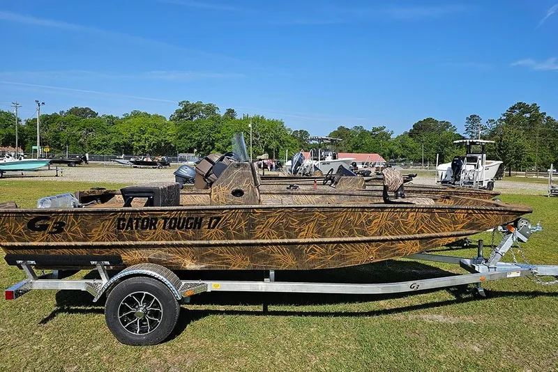 The Image of 2026 G3 Gator Tough 17 CC boat on trailer, camo design, parked outdoors. - 1