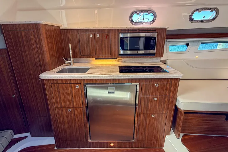 Slide: The Image of 2020 Pursuit OS 355 Offshore yacht kitchen with wood cabinetry, sink, microwave, and stove. - 25