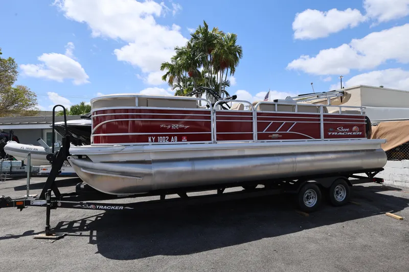 The Image of 2023 SUNTRACKER PB 22DLX pontoon boat on trailer under blue sky. - 1