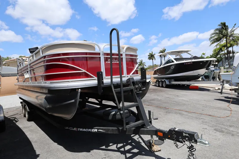 Slide: The Image of 2023 SUNTRACKER PB 22DLX pontoon boat on trailer, parked outdoors under blue sky. - 12